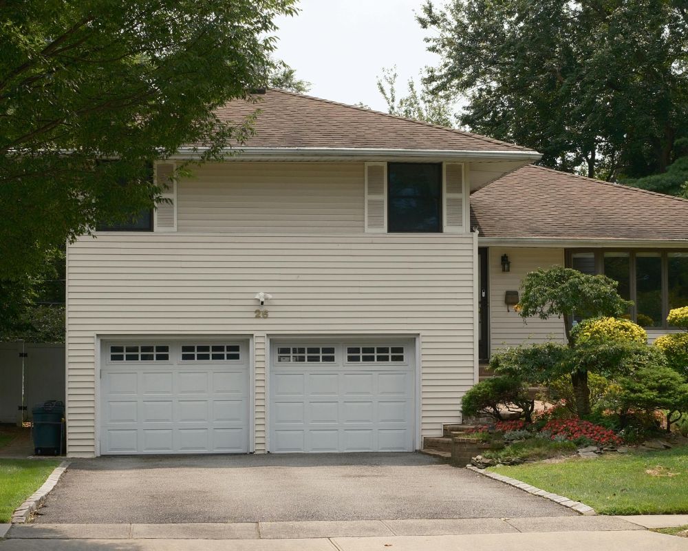 A Suburban House In Northwest Chicago Featuring Two Classic White Panelled Garage Doors With Window Inserts, Showcasing Popular Types Of Garage Doors For Residential Homes. The Installation Was Led By Contractor Dmytro Shevchenko Of Prime Garage Door Repair. The Image Captures A Clean, Traditional Look That Enhances Curb Appeal While Providing Essential Insulation For Illinois Winters.