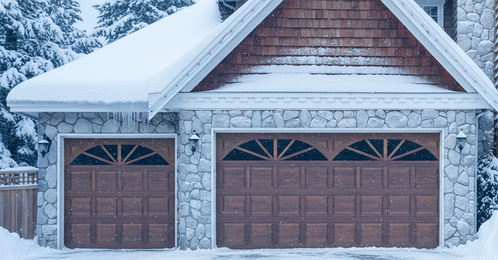 A Stone-Clad Home Covered In Heavy Snow, Featuring Elegant Carriage-House Style Wood-Finish Garage Doors With Arched Windows. This Winter Scene Showcases Durable And Stylish Garage Door Options Installed By Lead Contractor Dmytro Shevchenko For Homeowners In North West Chicago.