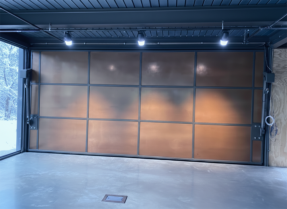  Interior View Of A Stunning Copper-Finished Garage Door Illuminated By Track Lighting, With A Snowy Winter Scene Visible Through The Large Side Window. This Custom Installation Showcases The Premium Garage Door Options Provided By Lead Contractor Dmytro Shevchenko For Clients In North West Chicago.