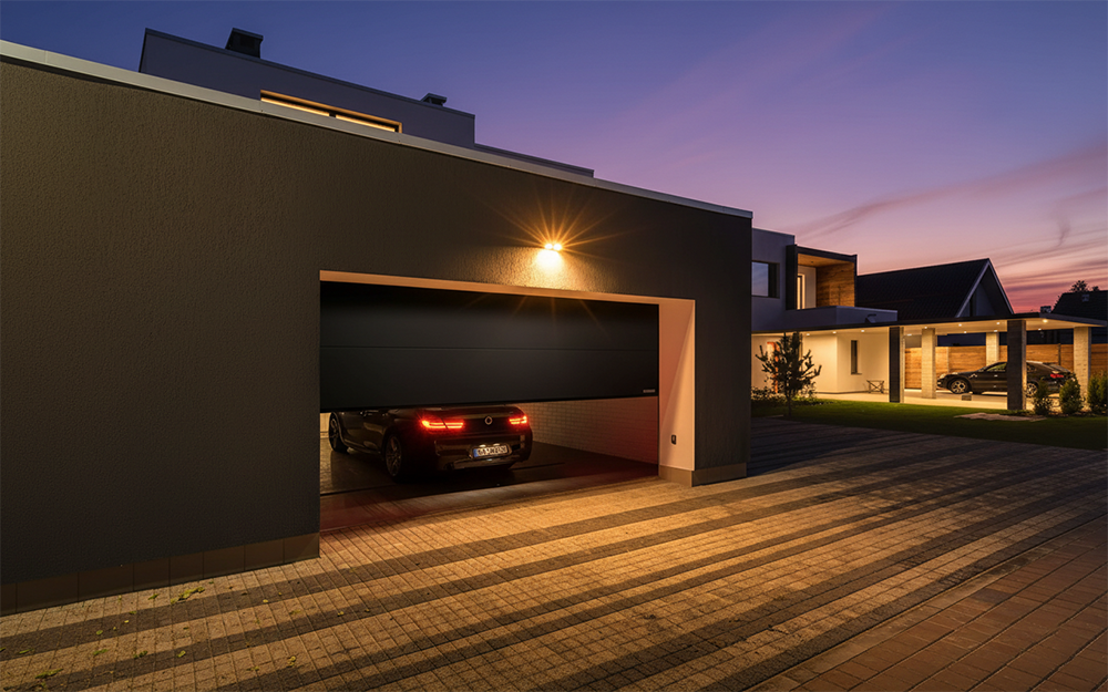 New Style Garage Doors: 2026 Trends &Amp; Modern Designs For Chicago Homes Contemporary Modern Home With Dark Charcoal Sectional Garage Door Partially Open, Luxury Black Sedan Parked Inside, Illuminated At Twilight With Warm Accent Lighting – Garage Door Options Installed By Lead Contractor Dmytro Shevchenko, North West Chicago