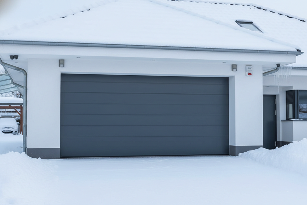 A Sleek, Dark Grey Sectional Garage Door Installed On A White Modern Home Amidst A Snowy Winter Landscape. This Image Showcases The Contemporary Garage Door Options And Professional Installation Services Provided By Lead Contractor Dmytro Shevchenko For Homeowners In North West Chicago.
