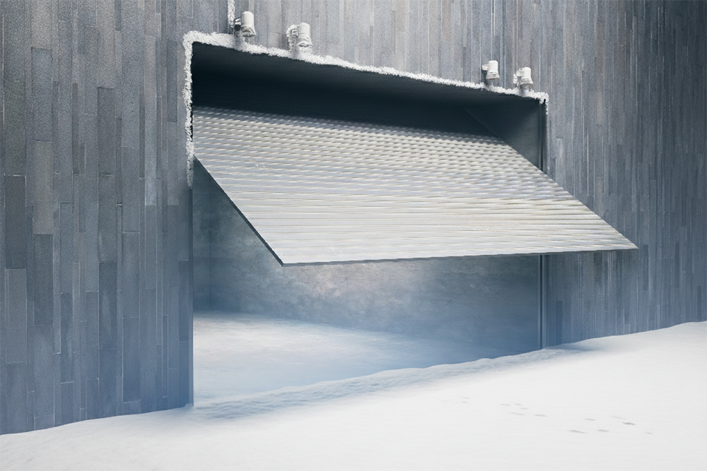A Sleek, Metallic Tilt-Up Garage Door Opening On A Modern Building With Dark Grey Tiled Walls, Set Against A Snowy Winter Background. This Distinctive Design Highlights The Unique Garage Door Options Available Through Lead Contractor Dmytro Shevchenko For Homes And Businesses In North West Chicago.