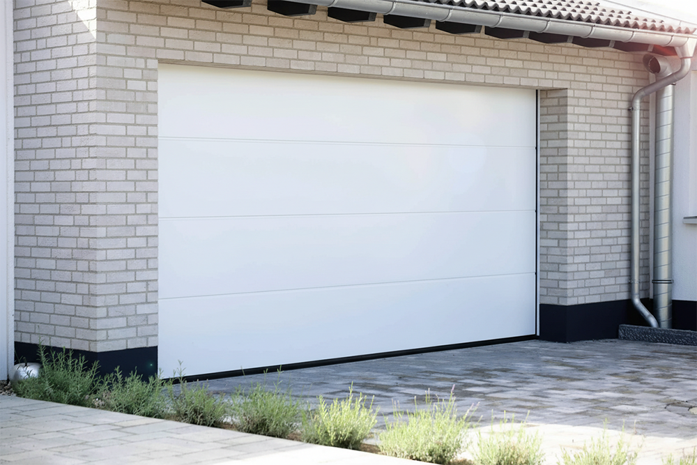 A Sleek, Modern White Sectional Garage Door Installed On A Light-Colored Brick House, Showcasing The Premium Garage Door Options Available From Lead Contractor Dmytro Shevchenko In The North West Chicago Area.