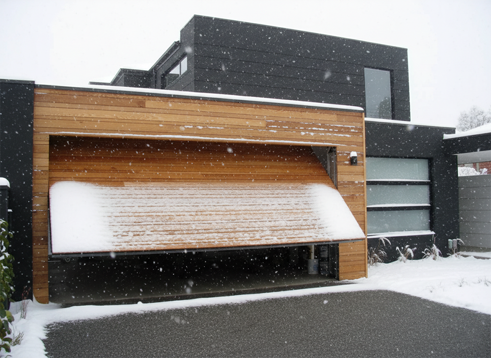A Sleek, Modern Black Home Featuring A Custom Natural Wood Tilt-Up Garage Door Partially Open During A Snowfall, Showcasing The Premium Garage Door Options Available From Lead Contractor Dmytro Shevchenko In The North West Chicago Area.