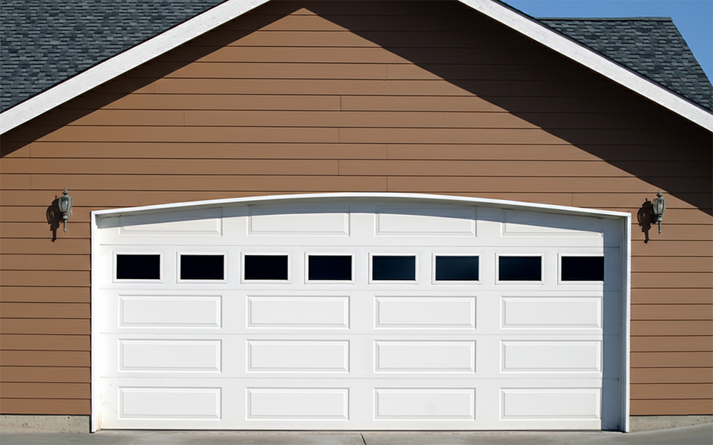 A Classic White Sectional Garage Door With Top Windows Installed On A Tan Residential Home, Showcasing The Various Garage Door Options Available From Lead Contractor Dmytro Shevchenko In The North West Chicago Area.