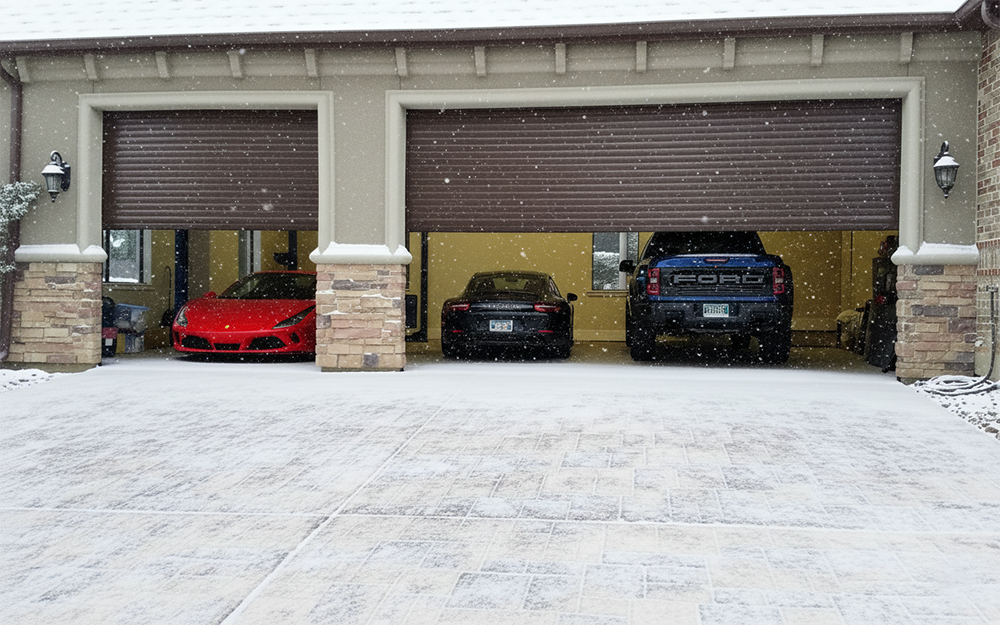 Brown Rolling Garage Doors Opening To Reveal Luxury Vehicles During A Snowfall, Showcasing Premium Garage Door Options Provided By Lead Contractor Dmytro Shevchenko For Homes In North West Chicago.