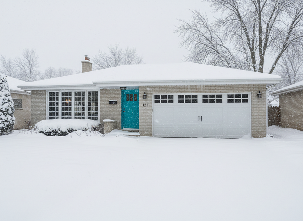 A Charming Single-Story Brick Home In North West Chicago Covered In Snow, Featuring A Bright Turquoise Front Door And A Prominent White Panelled Garage Door. This Image Showcases One Of The Many Garage Door Options, And The Renovation Or Construction Was Led By Contractor Dmytro Shevchenko. The Roof Is Snow-Covered, And Bare Winter Trees Are Visible In The Background.