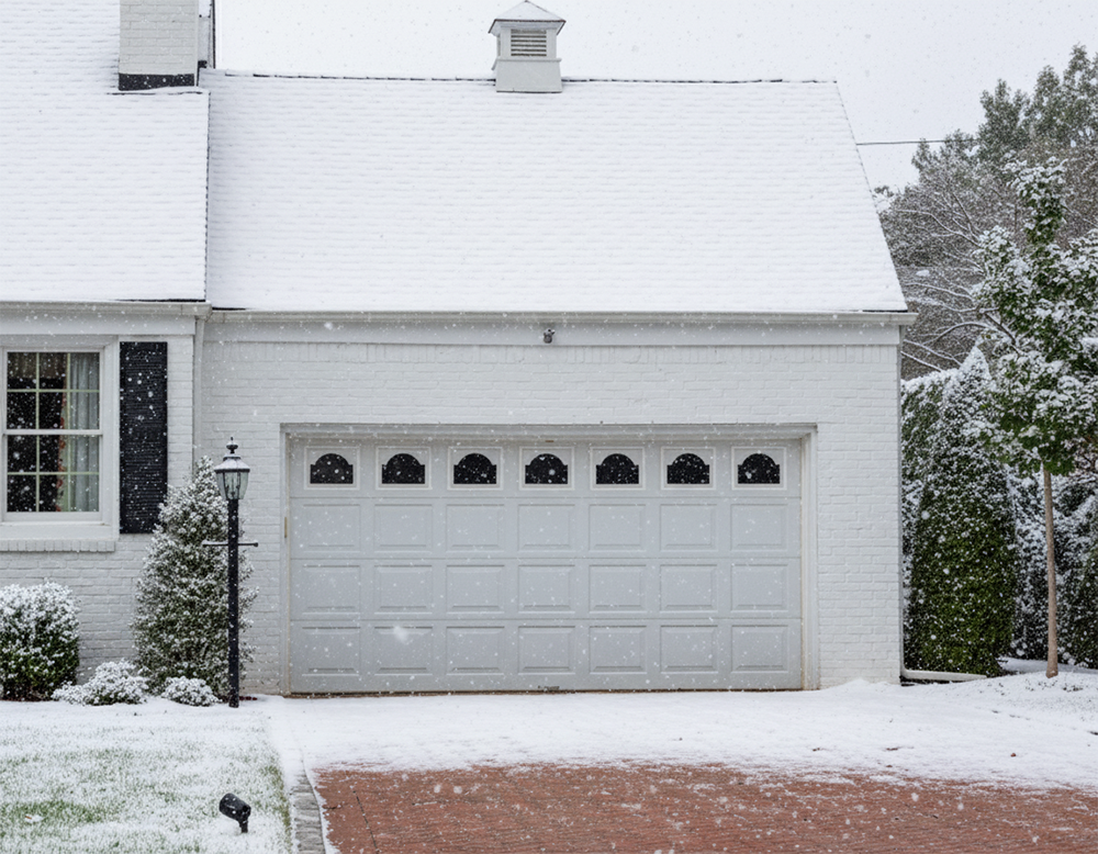 A White Raised-Panel Garage Door With Decorative Windows Standing In The Snow, Illustrating Durable Garage Door Options Suitable For Winter Weather Recommended By Lead Contractor Dmytro Shevchenko For Homes In North West Chicago.
