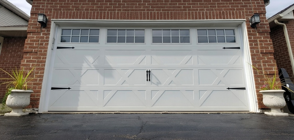 White Double Garage Door With Geometric Crisscross Raised Panel Design, Carriage-House Style Black Strap Hinges And Handles, And Four Rows Of Square Glass Windows, Installed On A Red Brick Suburban Home In North West Chicago. Garage Door Installation By Lead Contractor Dmytro Shevchenko.