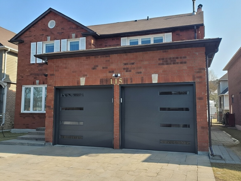 Modern Dark Gray Double Garage Door With Horizontal Recessed Panels And Slim Vertical Glass Inserts, Installed On A Red Brick Two-Story Home With Address 115 In North West Chicago. Garage Door Installation By Lead Contractor Dmytro Shevchenko.