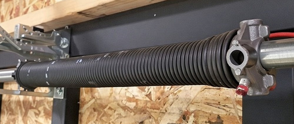 What Is A Garage Door Called? A Guide To Names And Terminology Close-Up Of A Garage Door Torsion Spring Assembly, Featuring A Black-Coated Torsion Spring Wound On A Steel Shaft With Winding Cone, Stationary Cone, And Secure Mounting Brackets, Part Of A Professional Overhead Garage Door System, Installed By Lead Contractor Dmytro Shevchenko In North West Chicago.