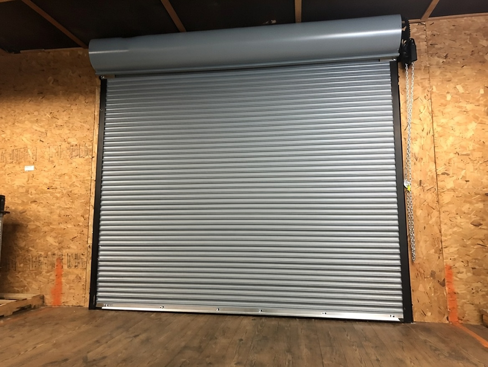 Residential Garage Door Types: A Complete 2026 Guide For Chicago Homeowners Interior View Of Fully Closed Gray Roll-Up / Rolling Residential Garage Door With Horizontal Aluminum Slats, Powder-Coated Grey Finish, Black Side Guides And Bottom Rail, Manual Chain Hoist Mechanism Visible, Installed In A Plywood-Lined Garage Space, North West Chicago. Lead Contractor Dmytro Shevchenko – Secure Residential Garage Door Types.