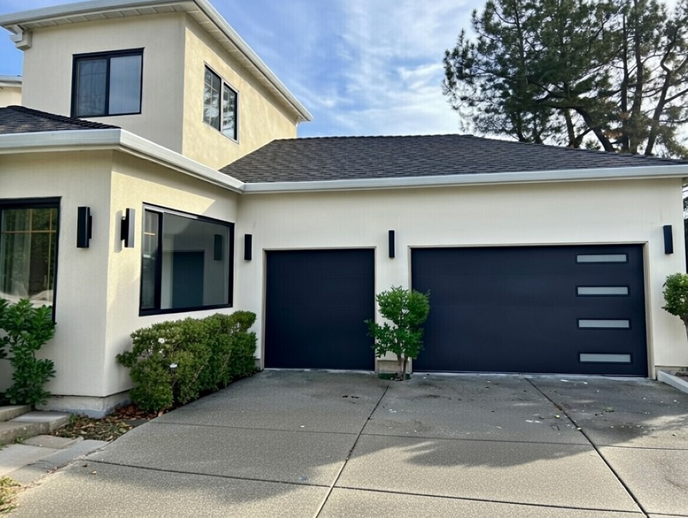 Modern Contemporary Home Exterior Featuring Two Dark Navy Blue Sectional Garage Doors With Horizontal Silver Accent Bars, Installed On A Beige Stucco Two-Story House With Black-Framed Windows And Sleek Wall Sconces – Garage Door Options By Lead Contractor Dmytro Shevchenko, North West Chicago