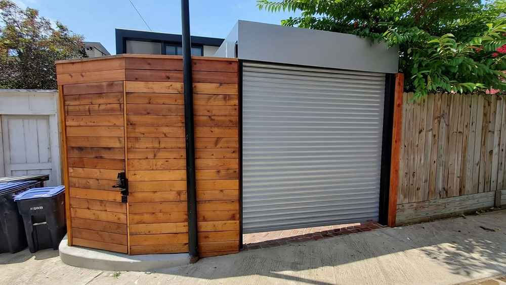 Residential Garage Door Types: A Complete 2026 Guide For Chicago Homeowners Modern Residential Side-Yard Setup Featuring A Silver Horizontal Slat Roll-Up Garage Door Paired With A Corner Cedar Wood Storage Shed Enclosure, Flat Grey Roofline, Black Trim Accents, Concrete Pad Base, Surrounded By Wooden Fence And Greenery, Sunny Outdoor View. North West Chicago. Lead Contractor Dmytro Shevchenko – Stylish Residential Garage Door Types.
