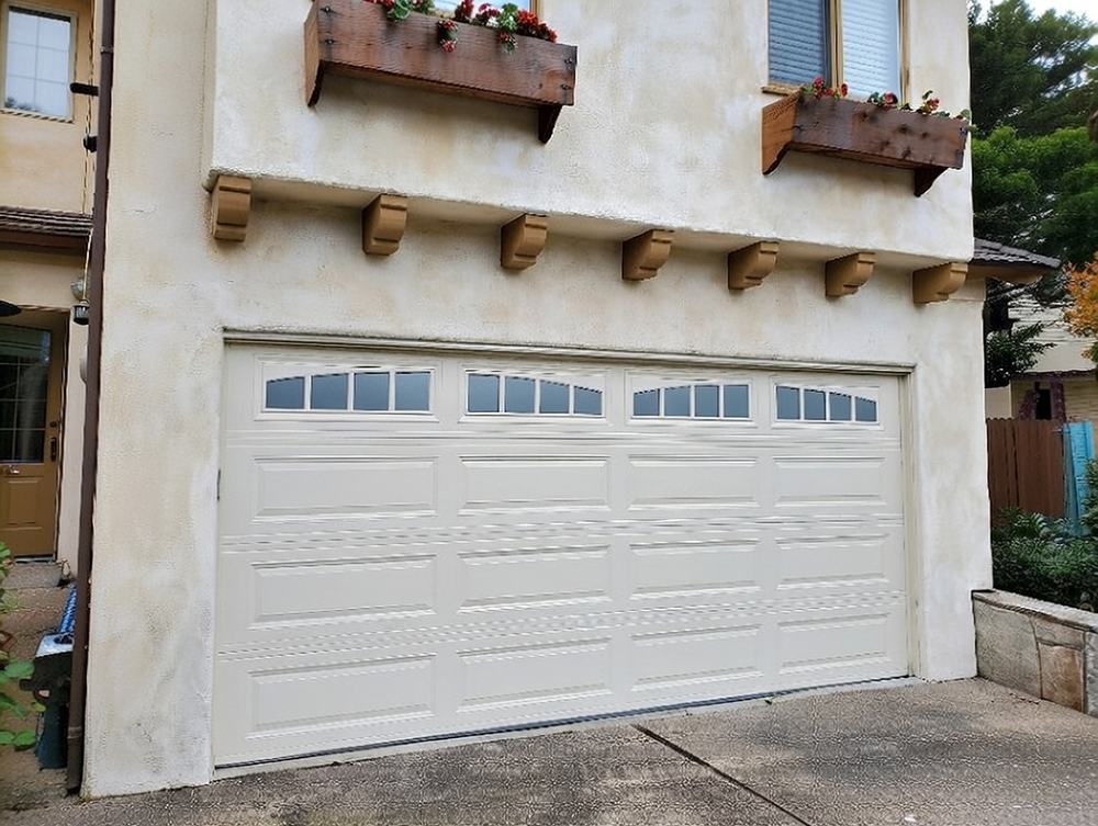 Traditional Garage Door Styles: The Timeless Choice For 2026 Traditional Garage Door Styles Featuring A Light Beige Raised-Panel Sectional Overhead Garage Door With Arched Multi-Pane Glass Windows Across The Top, Subtle Decorative Horizontal Banding, White Trim Frame, Mounted On A Two-Story Stucco Home With Wooden Flower Box Accents Filled With Red Blooms, Corbel Supports, And Mediterranean-Inspired Architecture, North West Chicago. Lead Contractor Dmytro Shevchenko – Timeless Traditional Garage Door Styles.