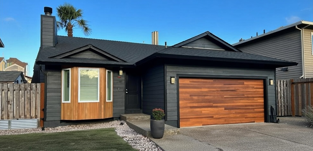 Traditional Garage Door Styles: The Timeless Choice For 2026 Traditional Garage Door Styles Featuring A Rich Cedar Wood-Look Sectional Overhead Garage Door With Horizontal Plank Texture And Warm Natural Grain Finish, Framed In Dark Grey Trim On A Modern Craftsman-Style Home With Charcoal Board-And-Batten Siding, Black Roof, Gabled Peaks, Wood Accent Entry, Palm Tree, Potted Plants And Gravel Landscaping Under Clear Blue Sky, North West Chicago. Lead Contractor Dmytro Shevchenko – Timeless Traditional Garage Door Styles.