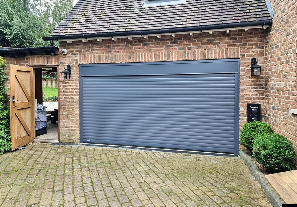 What Are The 5 Types Of Garage Doors? A 2026 Homeowner’s Guide Sleek Dark Grey Horizontal Slat Roll-Up Garage Door Fully Closed On A Traditional Red Brick Detached Garage With Tiled Pitched Roof, Black Trim Accents, Side Access Wooden Gate Open To Backyard, Wall-Mounted Lanterns And Security Camera, Lush Greenery And Brick-Paved Driveway – Example Of What Are The 5 Types Of Garage Doors. Lead Contractor Dmytro Shevchenko, North West Chicago.