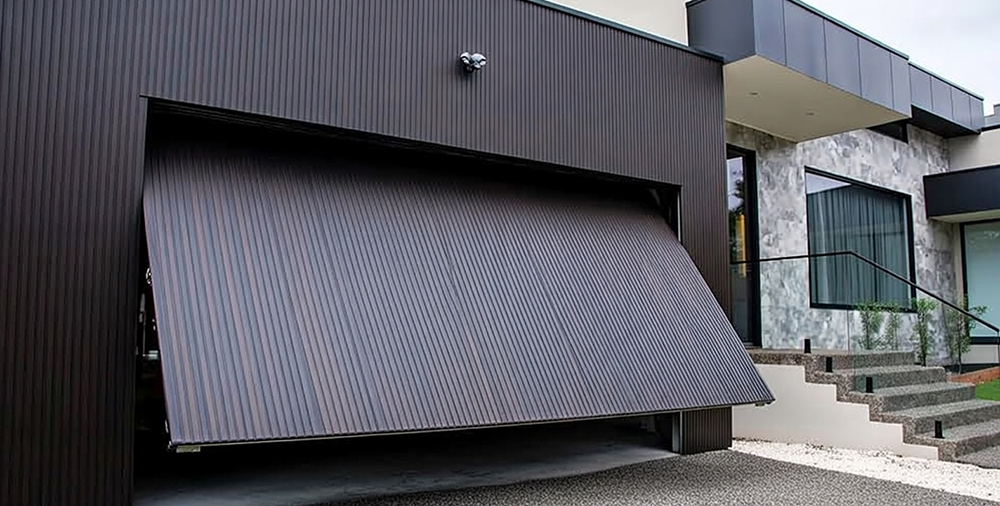 What Are The 5 Types Of Garage Doors? A 2026 Homeowner’s Guide Sleek Dark Brown Tilt-Up Canopy Garage Door In Partially Open Upward Position With Horizontal Ribbed Slats, Modern Flush-Mount Design On A Contemporary Dark-Clad Home Extension, Integrated With Stone-Tiled Steps And Minimalist Architecture, Dramatic Overhang Effect – One Of What Are The 5 Types Of Garage Doors. Lead Contractor Dmytro Shevchenko, North West Chicago.