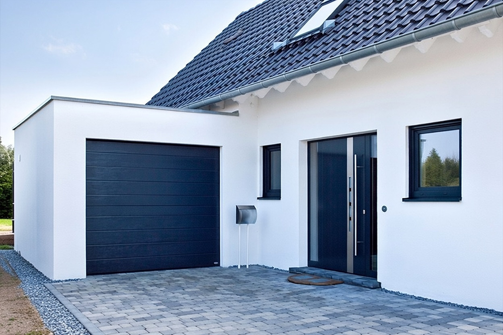 What Are The 5 Types Of Garage Doors? A 2026 Homeowner’s Guide Sleek Modern Single-Car Residential Home With Matte Black Horizontal Slat Sectional Garage Door Installed Flush On A Minimalist White Stucco Facade, Flat Grey Roof Extension, Dark-Framed Windows And Front Door, Contemporary European-Style Architecture With Gravel Driveway And Stone Pavers – Example Illustrating What Are The 5 Types Of Garage Doors. Lead Contractor Dmytro Shevchenko, North West Chicago.